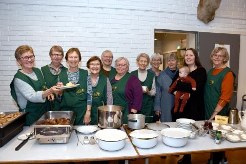 Kjøkengjengen frå Hyen bygdekvinnelag poserer ved serveringsdisken med ein tallerk med julemiddag.
