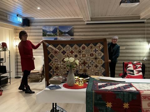 To damer frå Gloppen Quilteklubb held opp eit stort lappeteknikk-teppe mellom seg.