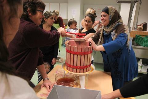 Samling rundt eplepressa: Ghazala Ibrahim og Awaz Hamed fra Syria, og Alyaa Makhzumi fra Irak var ivrig ved eplepressa. Det ble mye latter da det etter hvert ble en tung jobb å presse ut safta. Foto: Ragnhild Bakke.