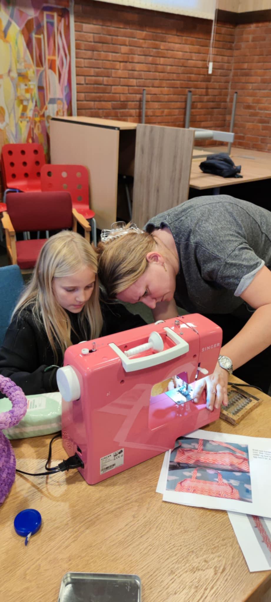 Barn og vaksen bøygd over rosa symaskin