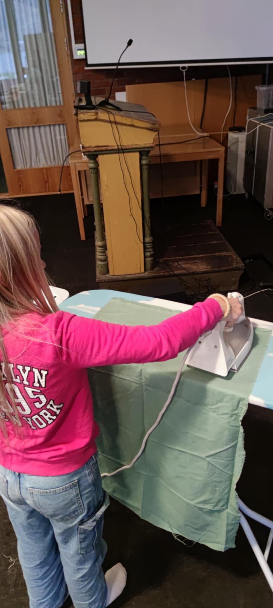 Jente stryk eit plagg ved sybord