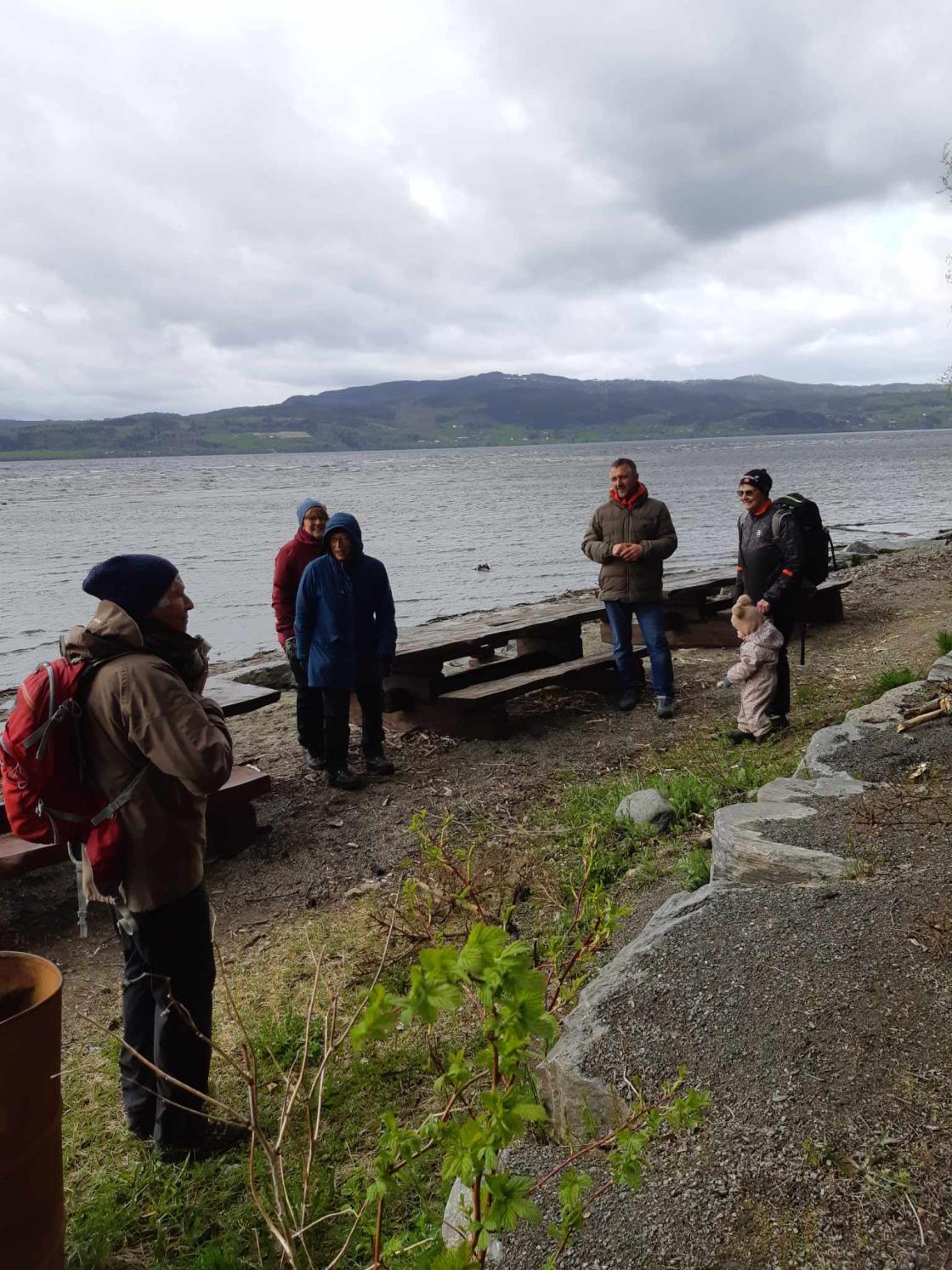 Folk står og prater ved benker ved vatn