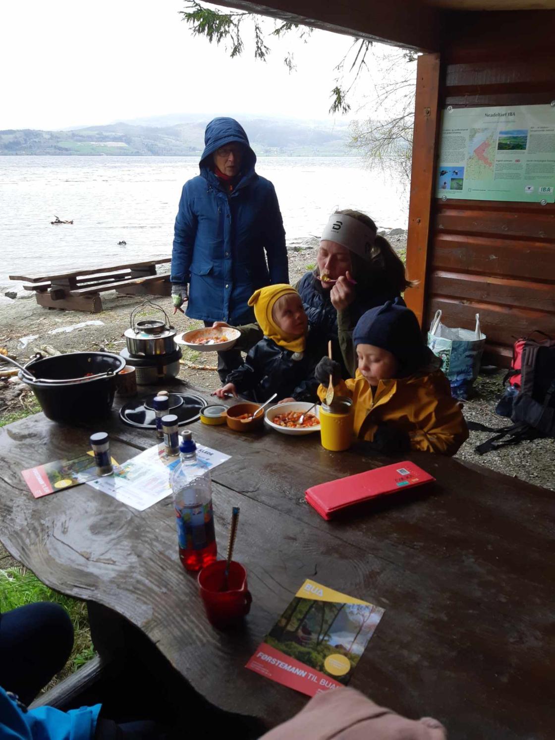 Voksne og barn spiser mat i gapahuk
