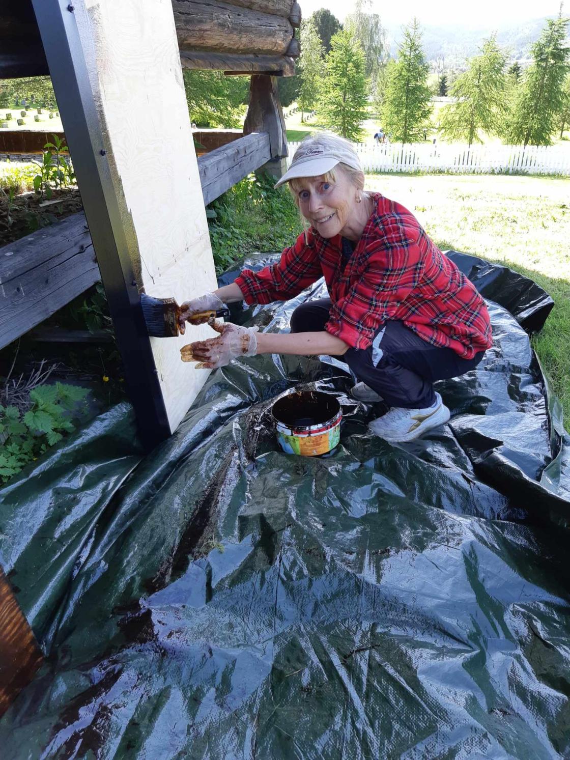 Kvinne sitter og maler/beiser benk