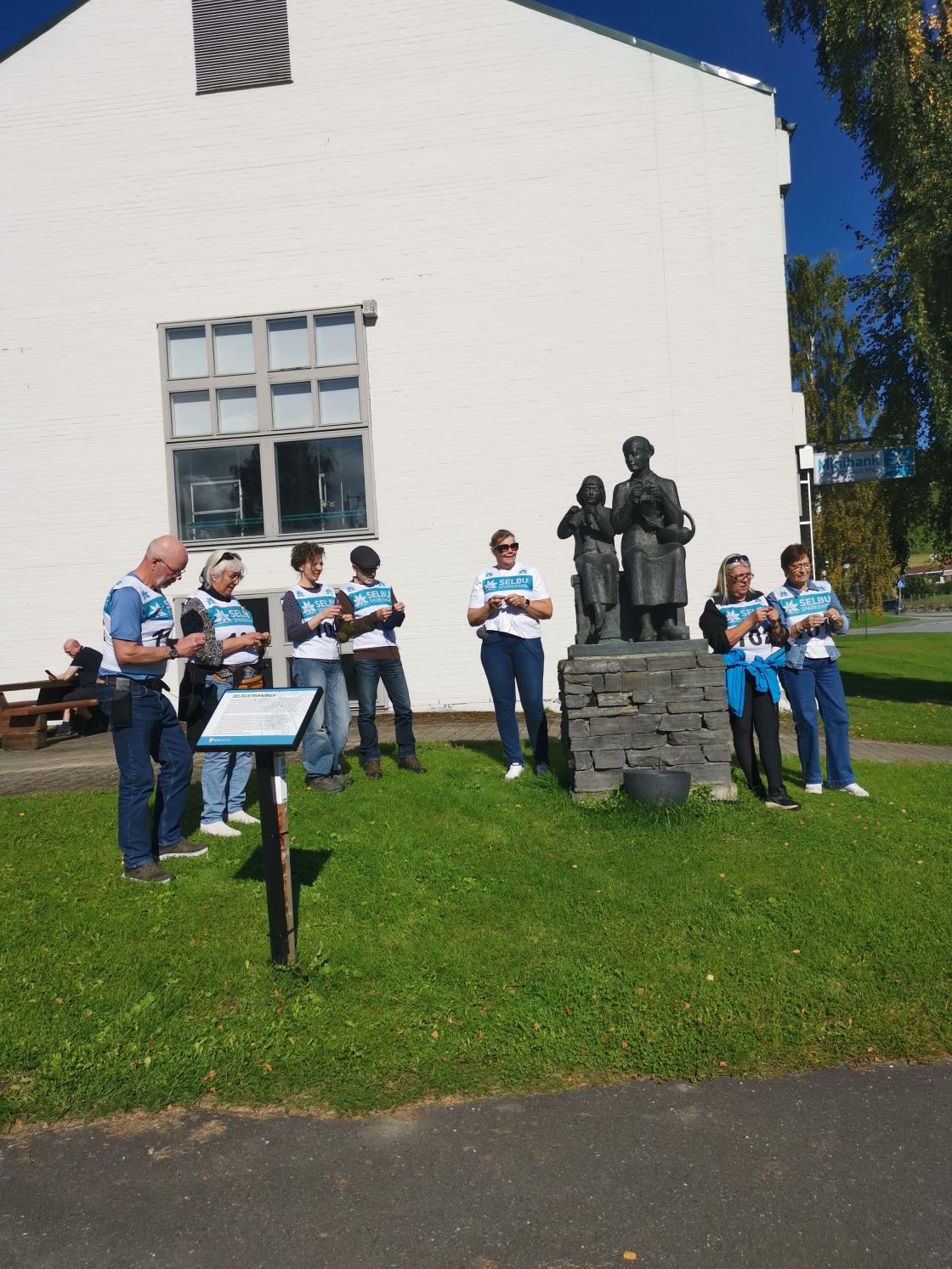 deltagere i gåstrikk står ved statue